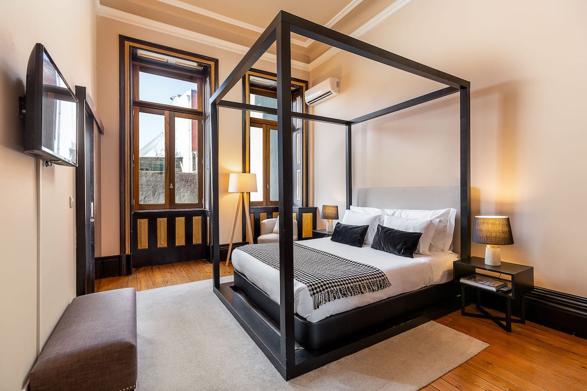 A four-poster bed with a black frame, a bedside table with a lamp, and a TV mounted on the wall.
