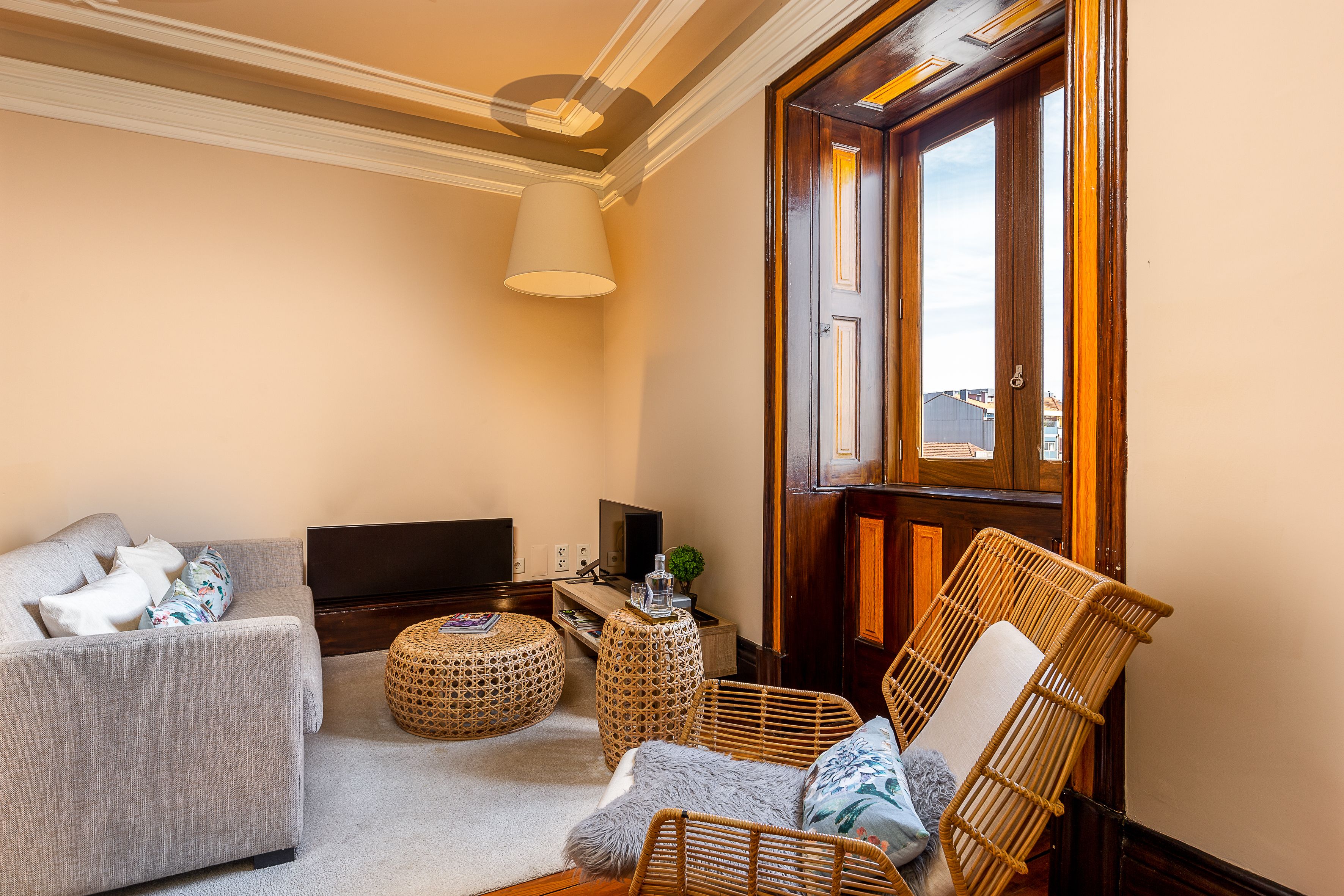 A living room with a sofa, two wicker chairs, a round ottoman, a television, and a wooden door.