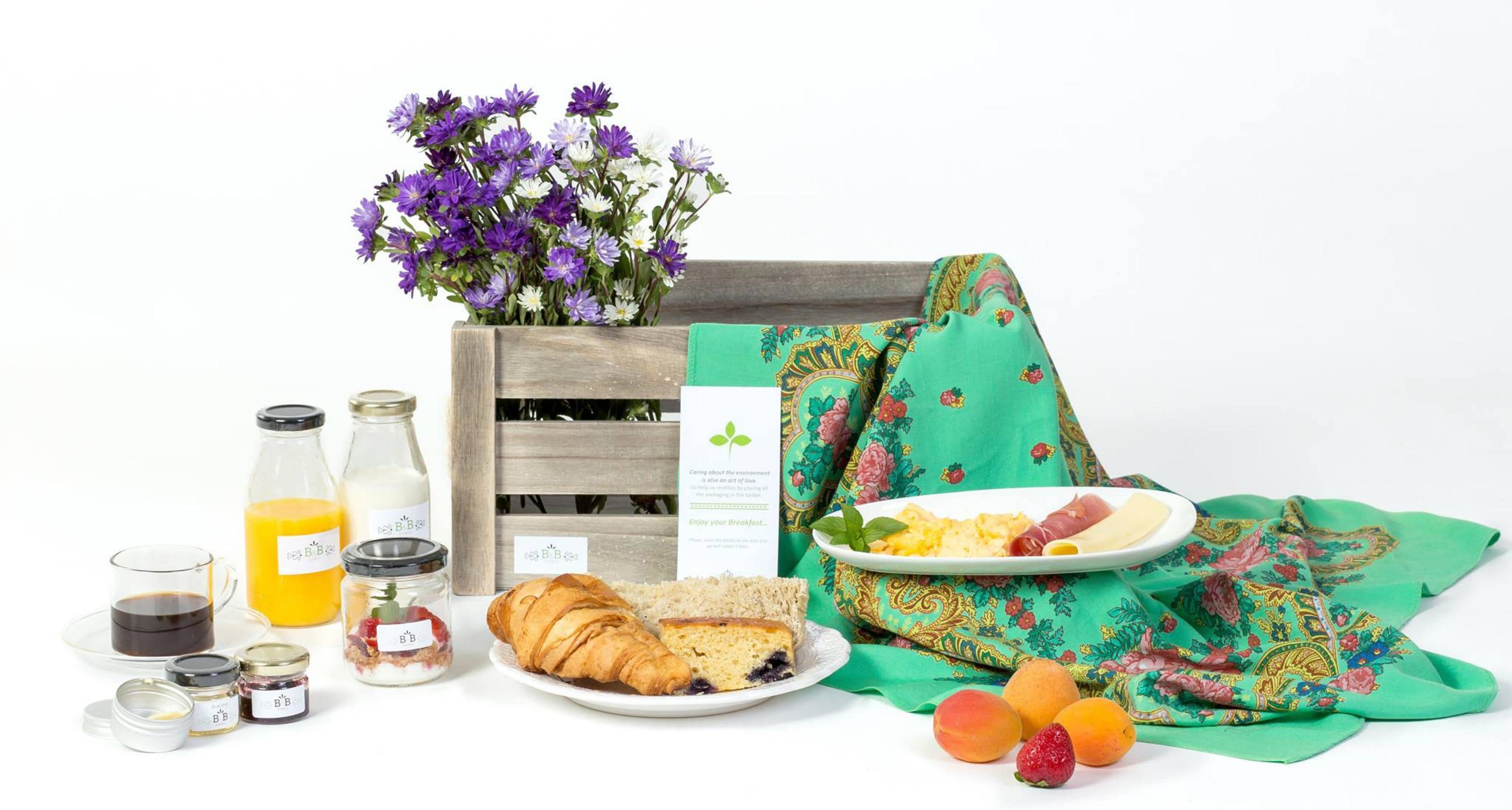 A breakfast setup with a croissant, fruit, and a plate of scrambled eggs and ham, along with a bottle of orange juice and a glass of coffee.