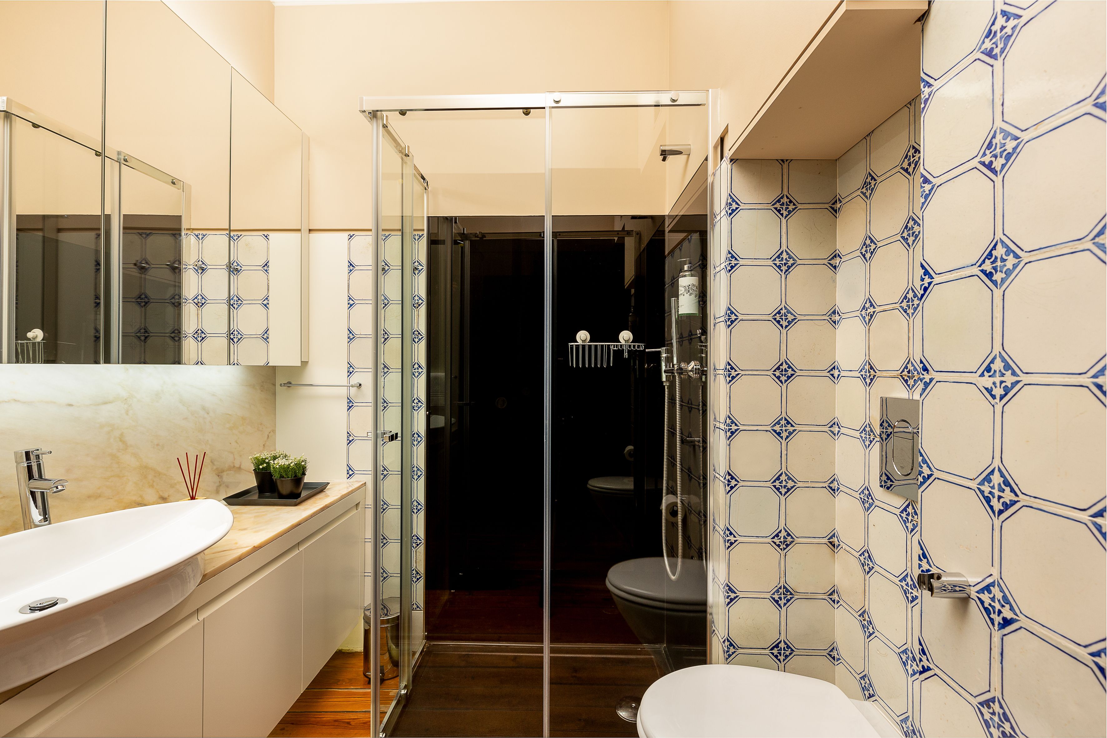 A bathroom with a glass shower enclosure, a sink with a marble countertop, and a toilet.