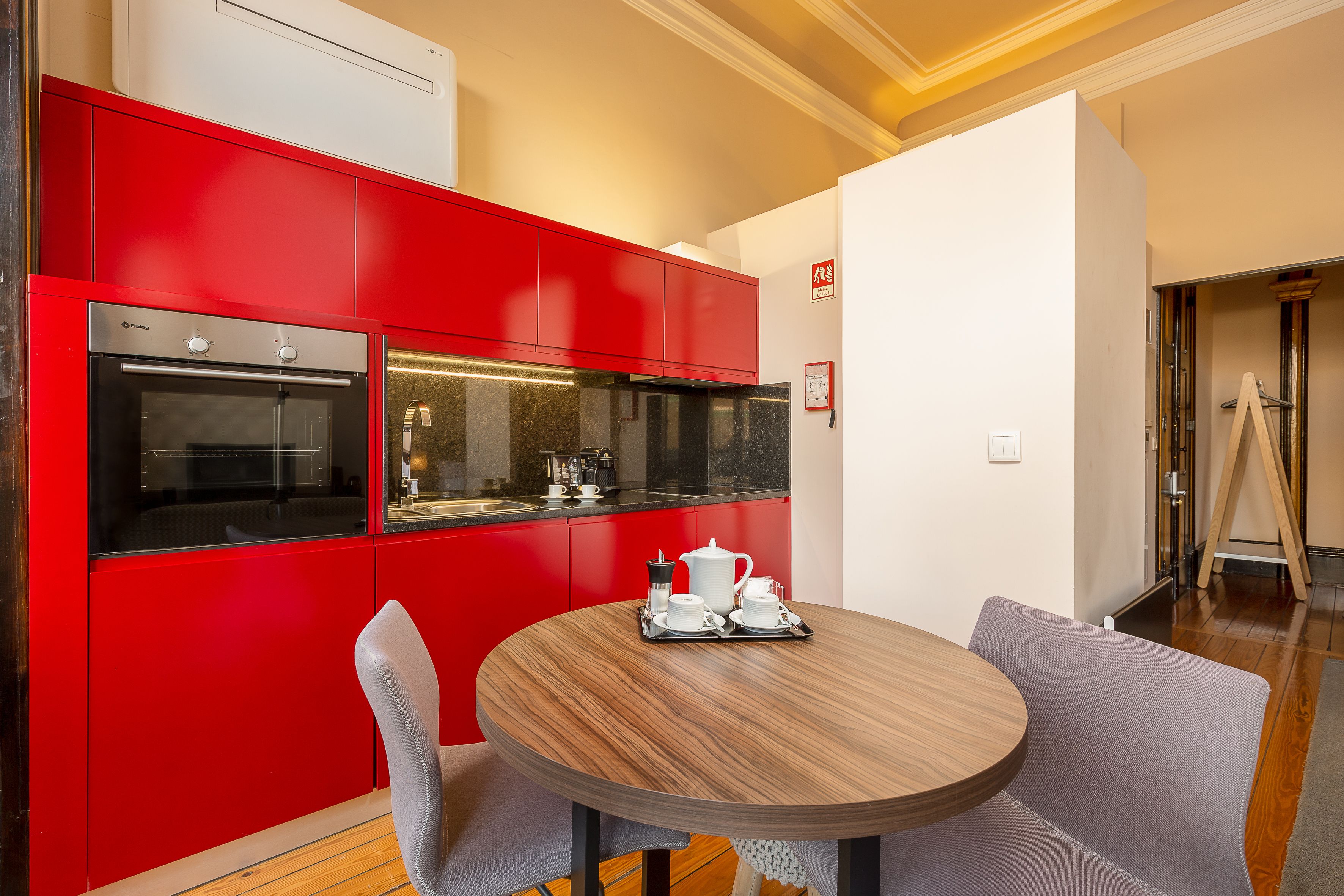 A modern kitchen with red cabinetry and a round wooden table with a coffee set.