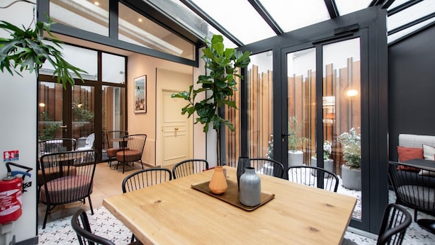 A modern dining area with a wooden table, black chairs, and potted plants. - Hôtel de l'Espérance (Paris)