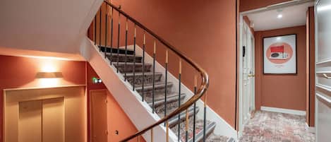 Una escalera con barandilla de madera, peldaños alfombrados y una pared con un cuadro enmarcado.