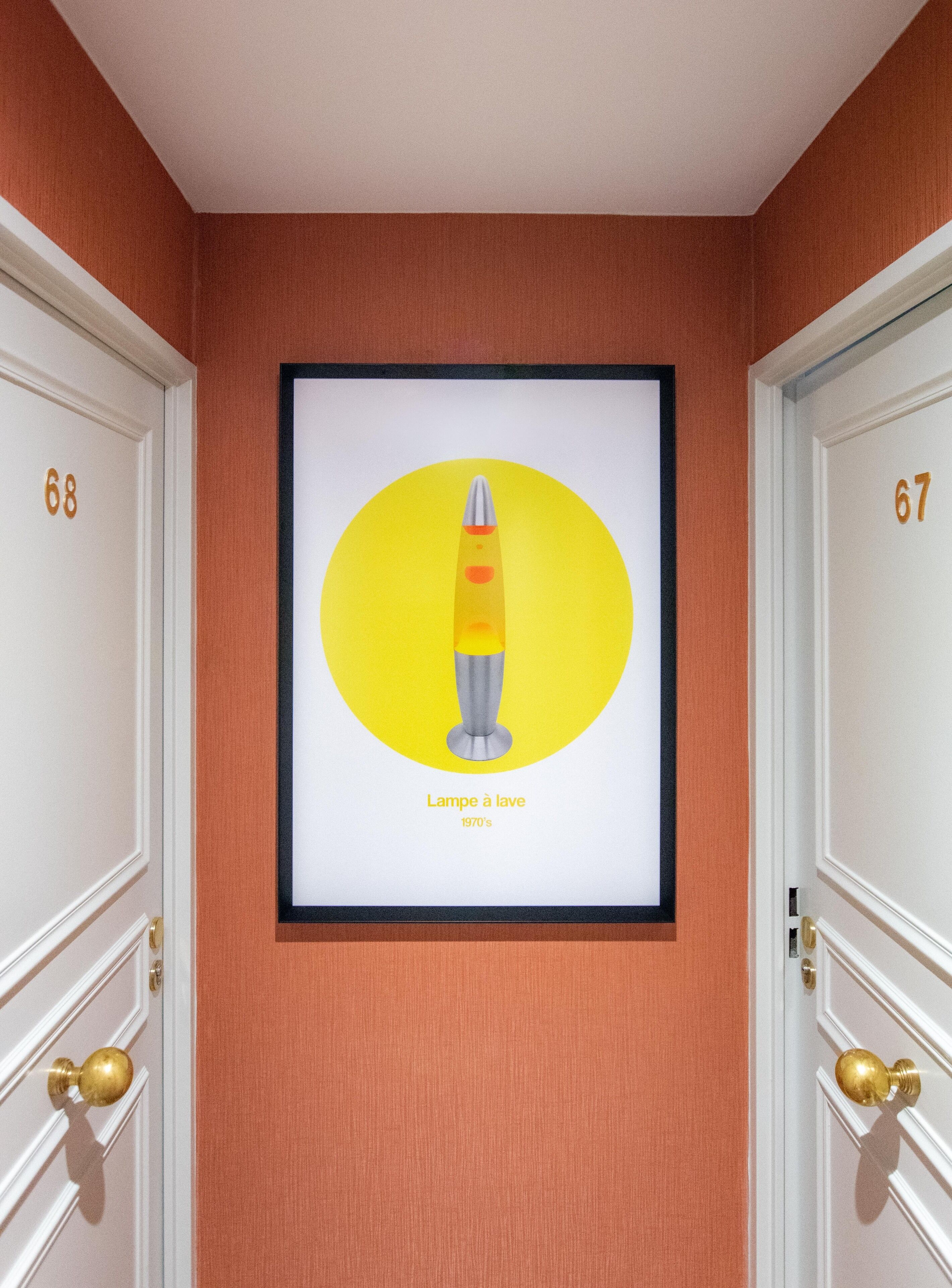 A framed artwork of a rocket on a wall between two doors labeled 67 and 68.