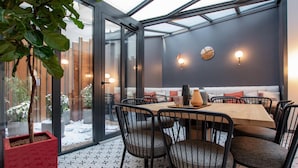 A modern dining area with a glass wall, a wooden table, and black chairs. - Hôtel de l'Espérance (Paris)