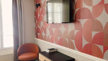Una habitación moderna con piso de madera, un escritorio negro con cajones, una silla roja, un televisor montado en la pared y un papel tapiz con círculos.