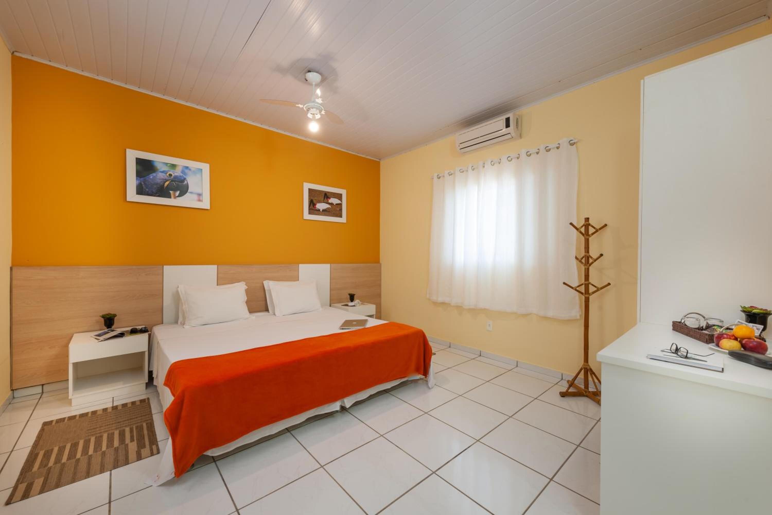A hotel room with a bed, a nightstand, a desk, a coat rack, and a window with curtains.