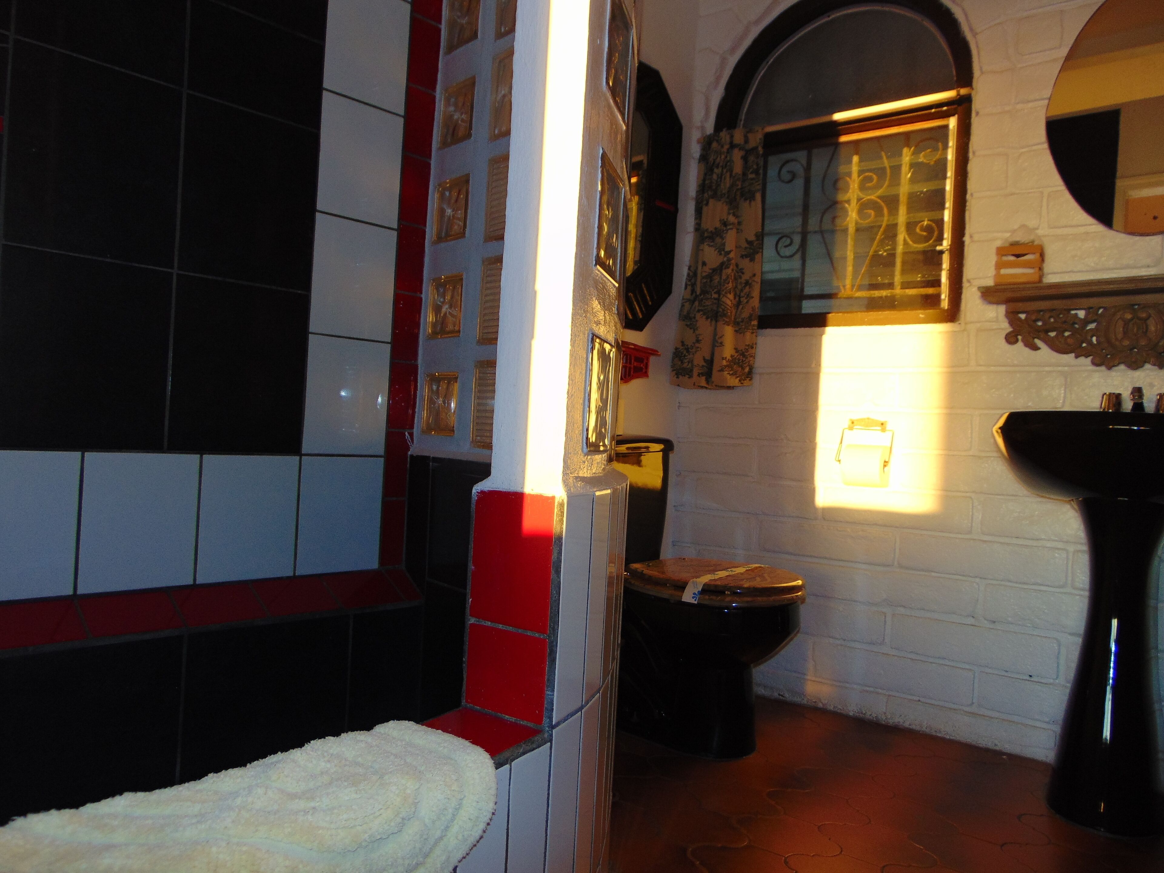 Un baño con pared de azulejos blancos, lavamanos negro y inodoro de madera.