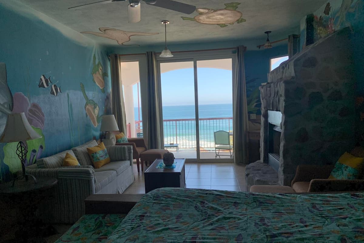 A room with a bed, a sofa, a chair, a table, and a view of the ocean.