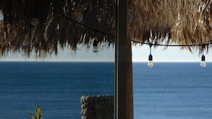 Vista al océano a través de una ventana con techo de paja y bombillas colgantes.