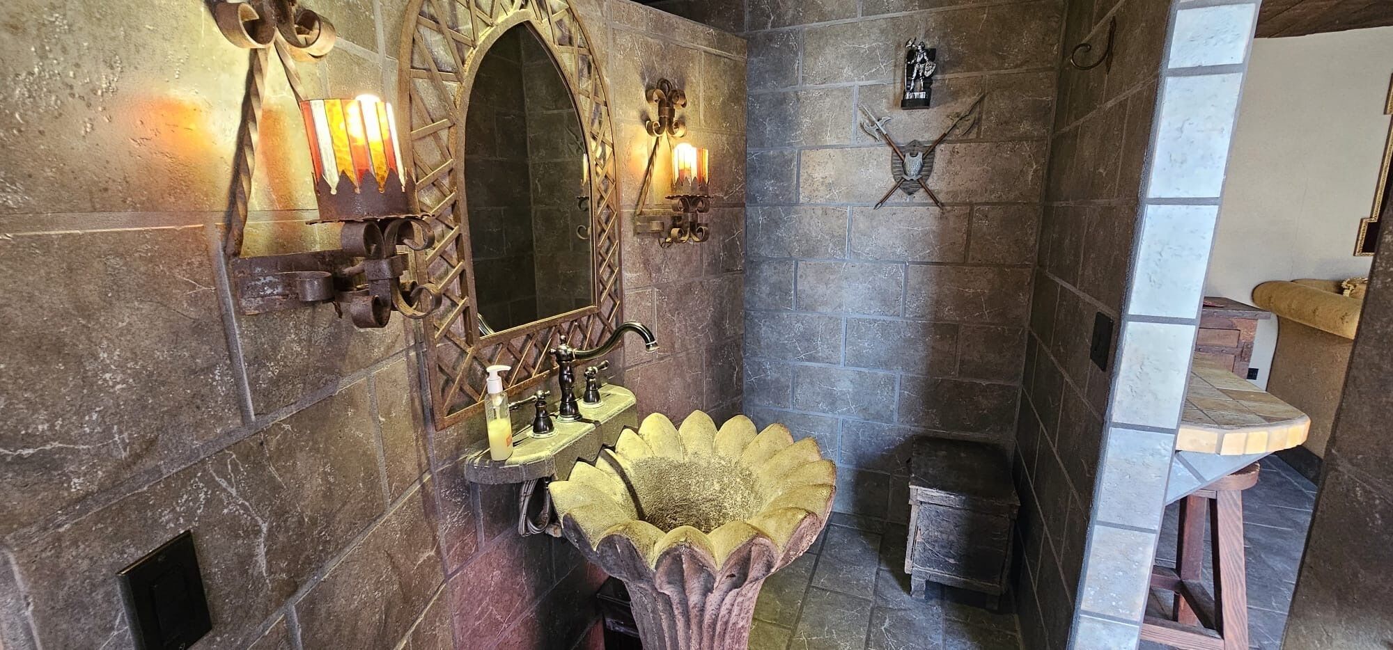 Une salle de bain aux murs en pierre, avec un lavabo d’époque et des appliques murales.