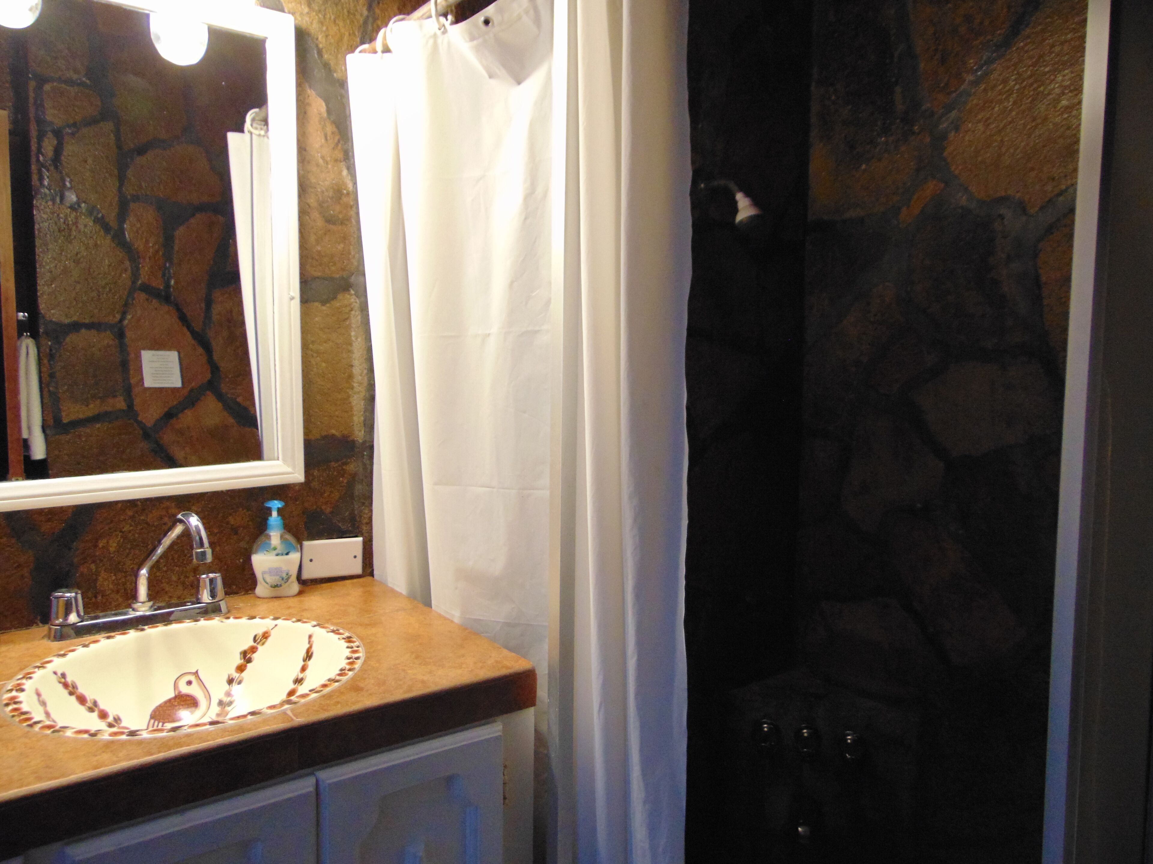 A bathroom with a stone wall, a sink with a decorative basin, a mirror, and a shower curtain.
