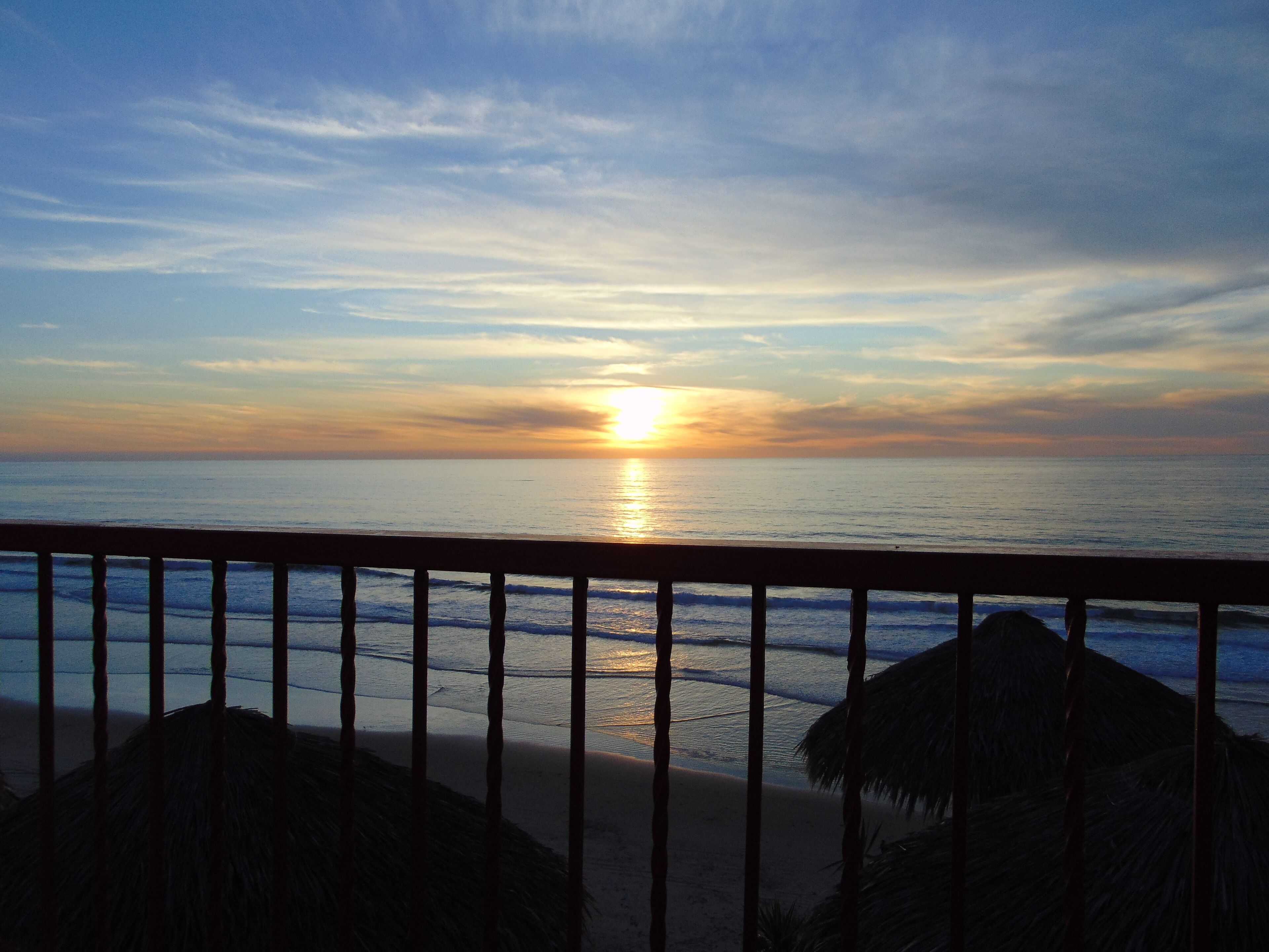 A sunset over the ocean with a wooden railing in the foreground.