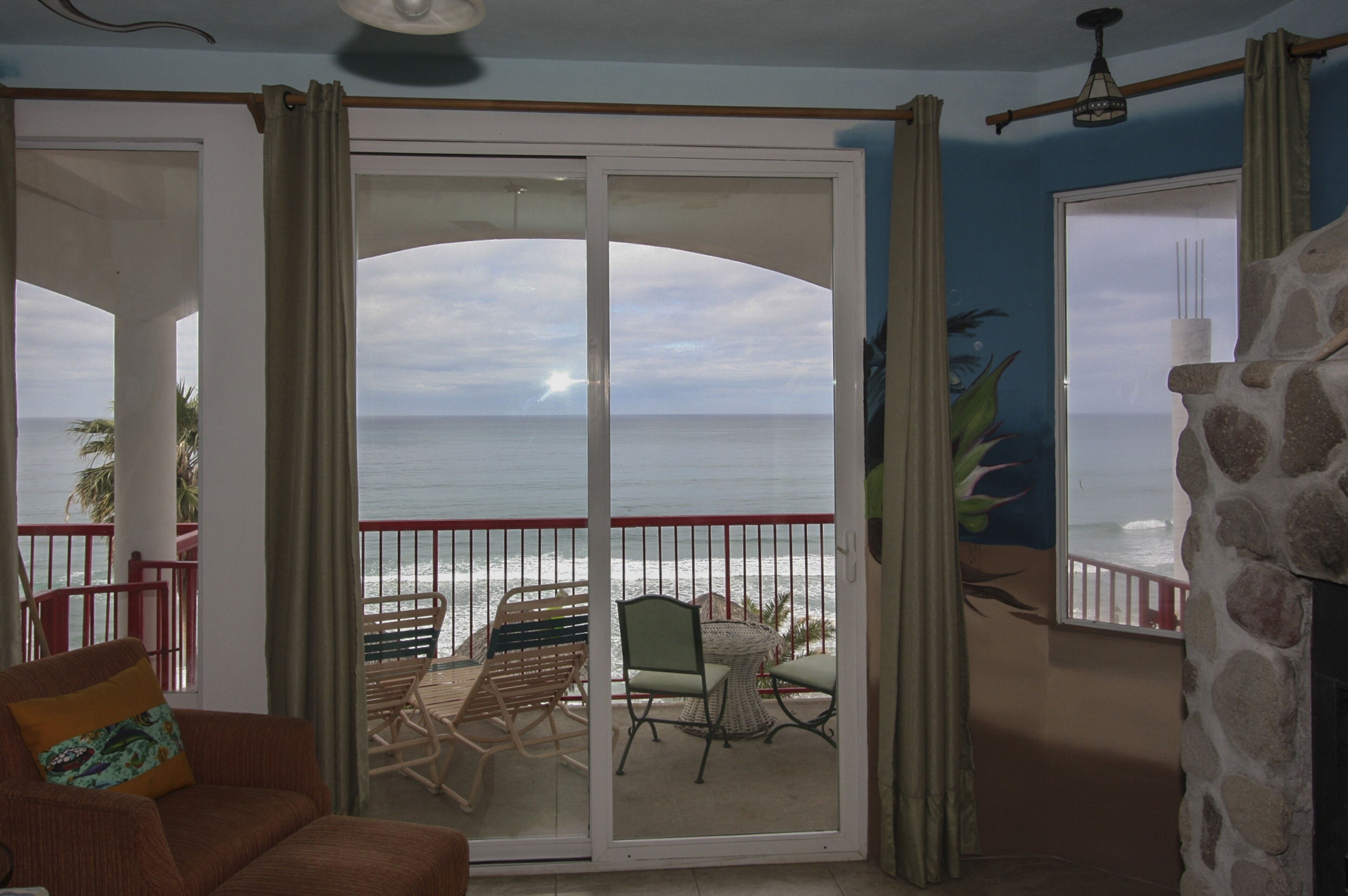 A room with a view of the ocean through a sliding glass door, a dining area with chairs and a table, and a stone fireplace.