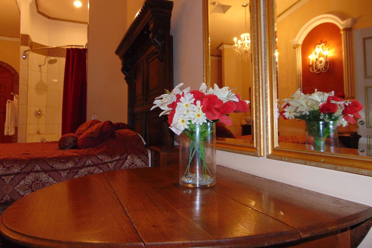 A hotel room with a wooden table, a mirror, and a vase of flowers.
