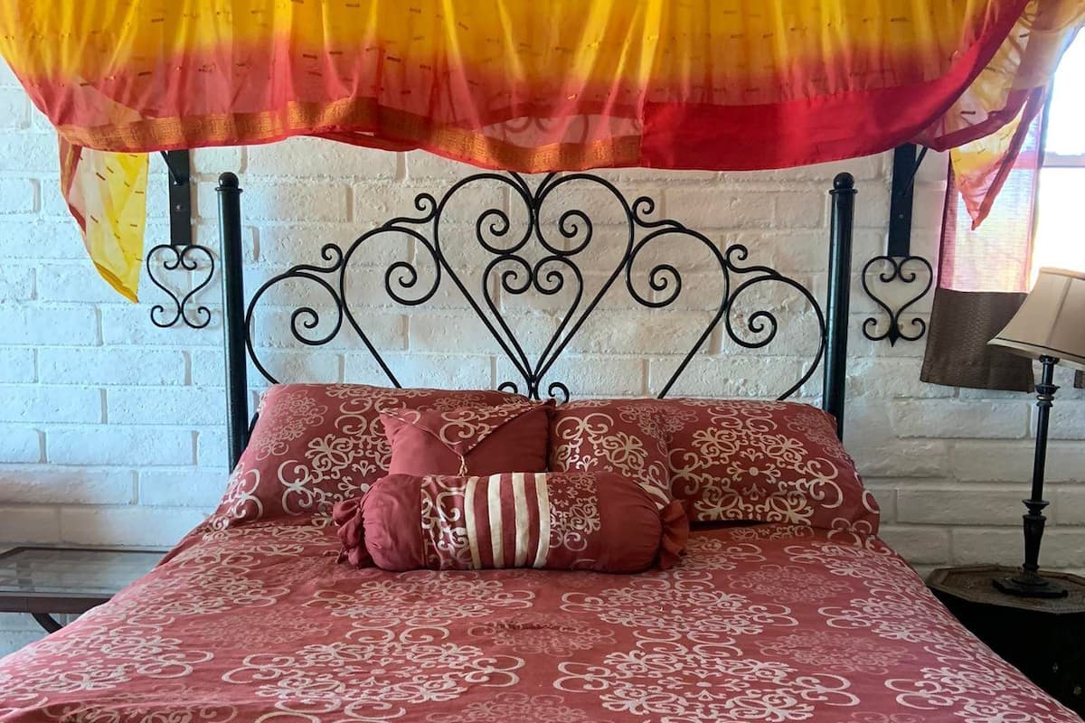 A bed with a patterned red and beige bedspread, a canopy with yellow and red drapes, and a metal headboard.