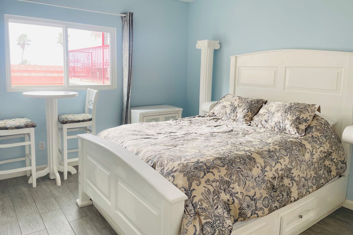 A bedroom with a bed, a small table, two chairs, a window, and a nightstand.