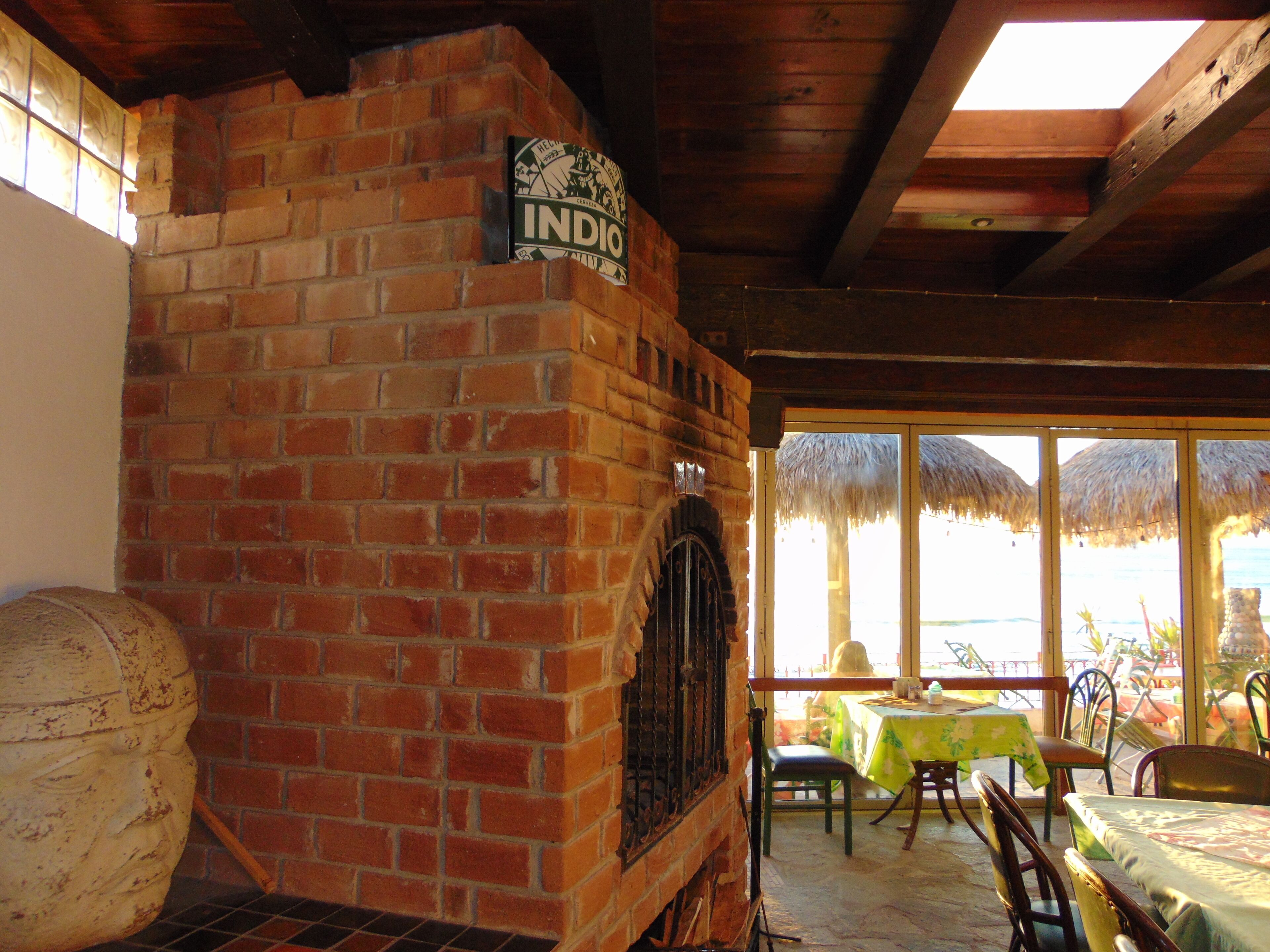 A brick oven labeled "INDIO" in a dining area with a view of the beach through large windows.