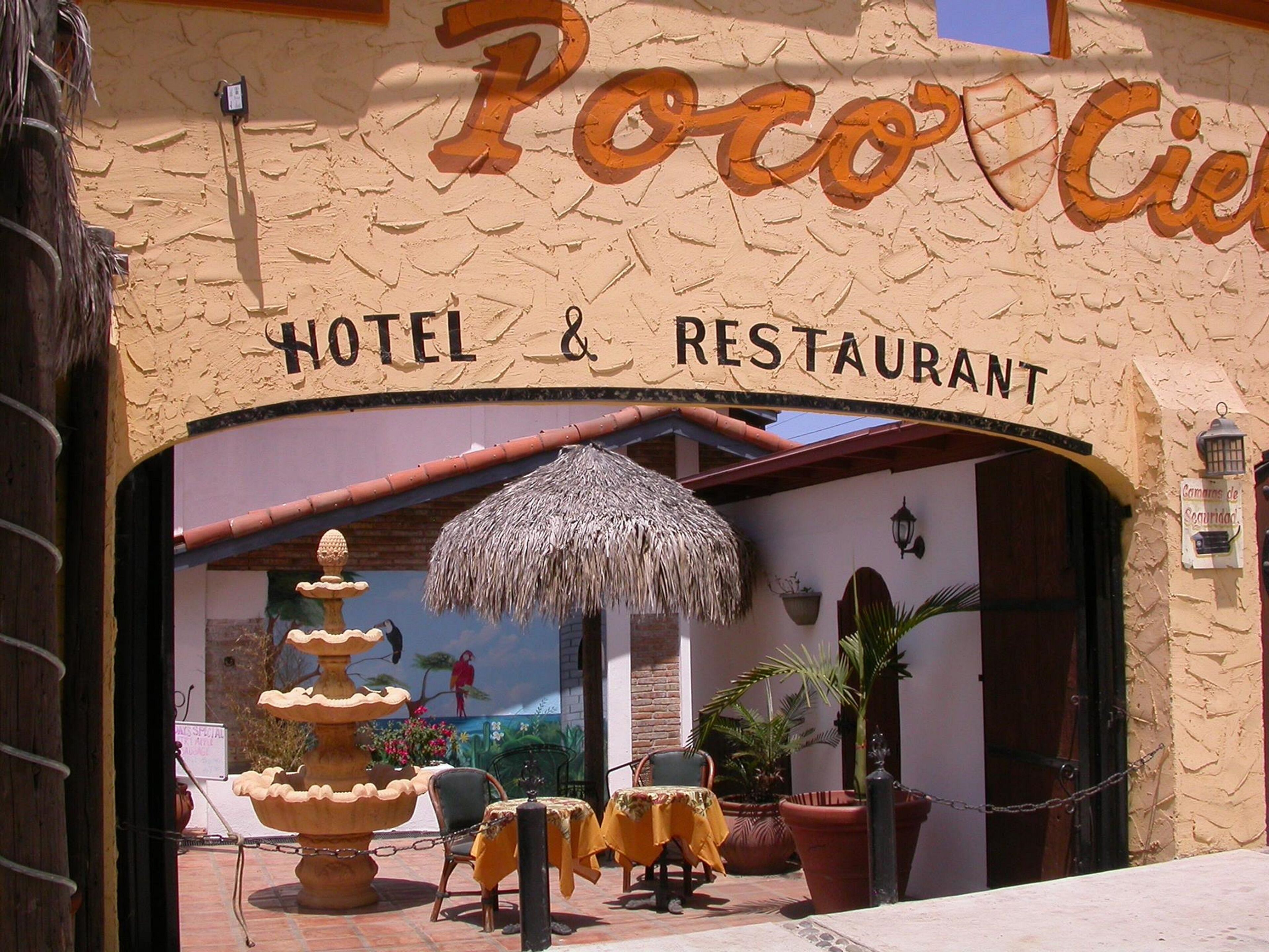 The entrance to Poco Cielo Hotel & Restaurant with a thatched umbrella, outdoor seating, and a decorative fountain.