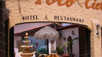 The entrance to Poco Cielo Hotel & Restaurant with a thatched umbrella, outdoor seating, and a decorative fountain.