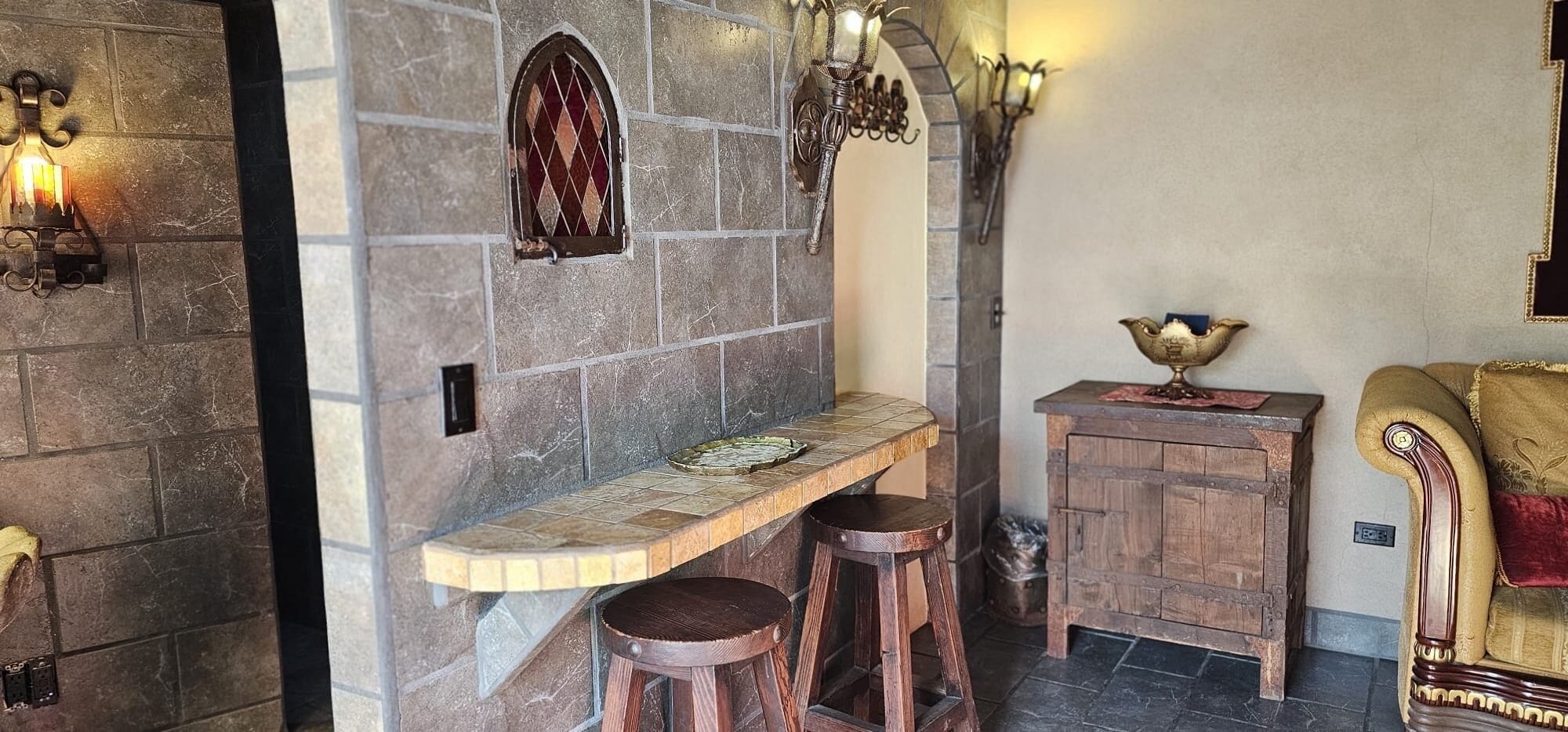 A stone-walled bar area with stools, a wooden counter, and a decorative cabinet.