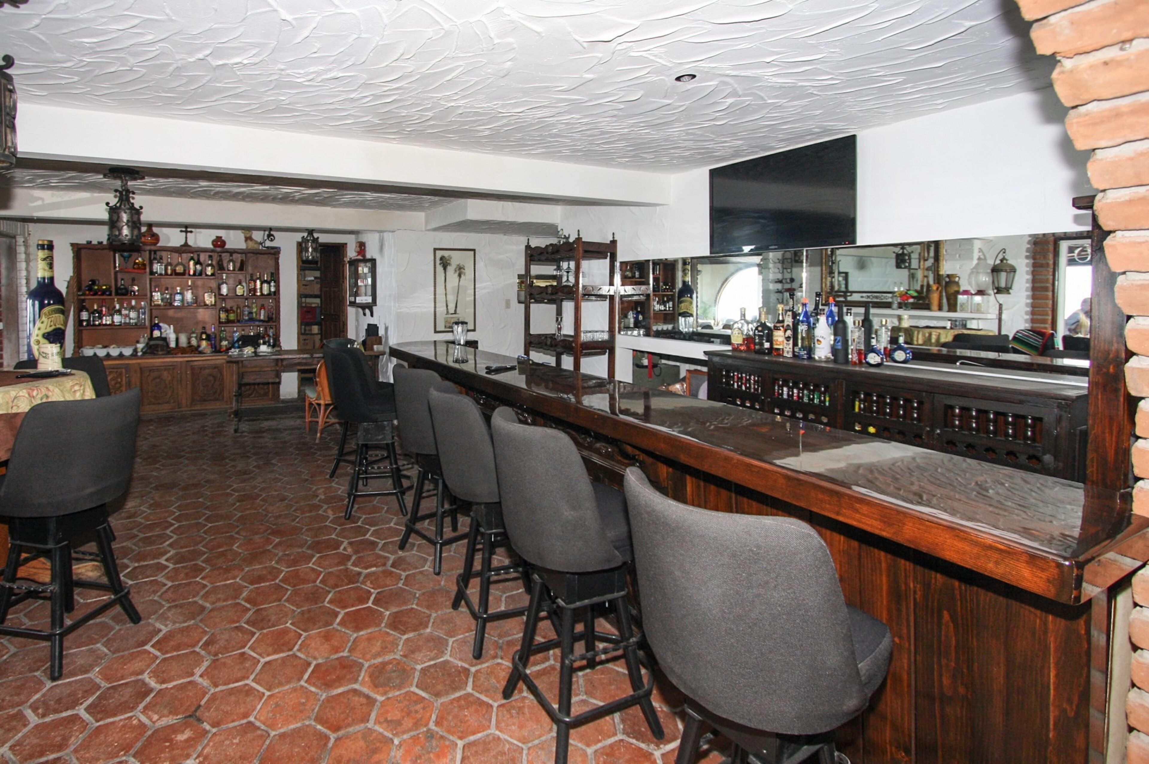 Una zona de bar con una barra larga, varios taburetes y estantes llenos de botellas.