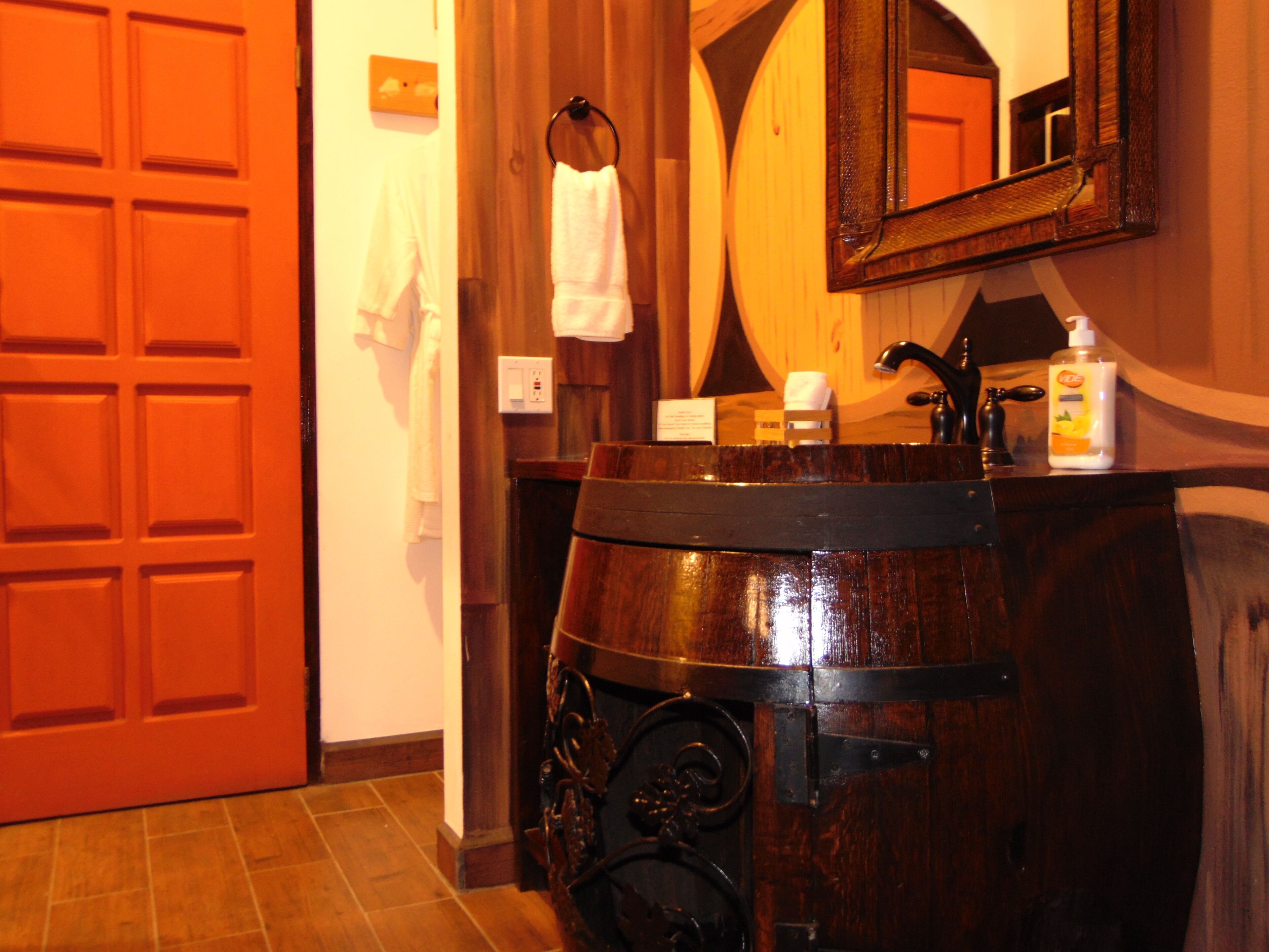 Un baño con un lavabo de barril de madera, un espejo y un perchero para toallas.