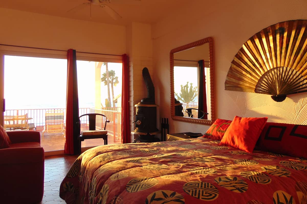 A hotel room with a bed, a ceiling fan, a large mirror, and a balcony with a view of palm trees.