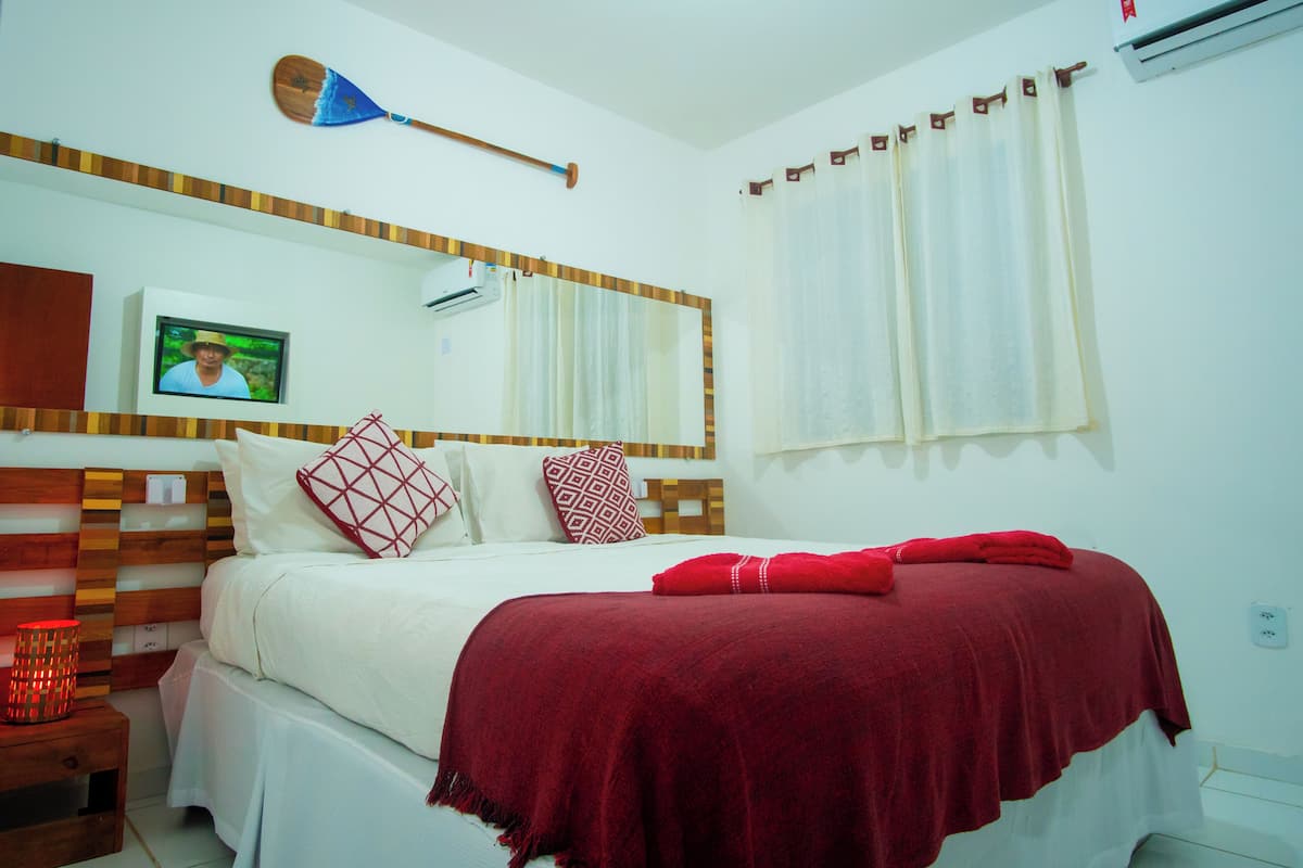 Habitación de hotel con cama, televisión montada en la pared, cabecera de madera y ventana con cortinas.