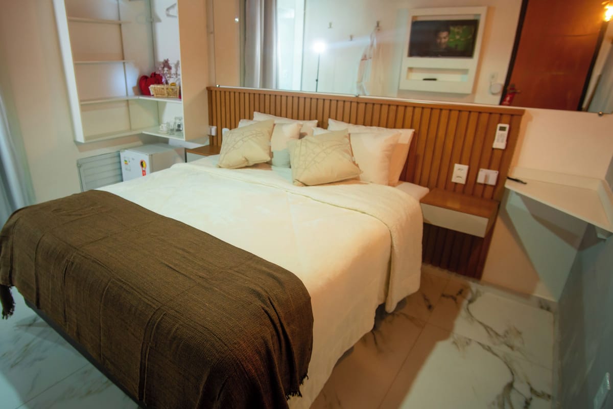 Una habitación de hotel con cama, mesita de noche, espejo y televisión.