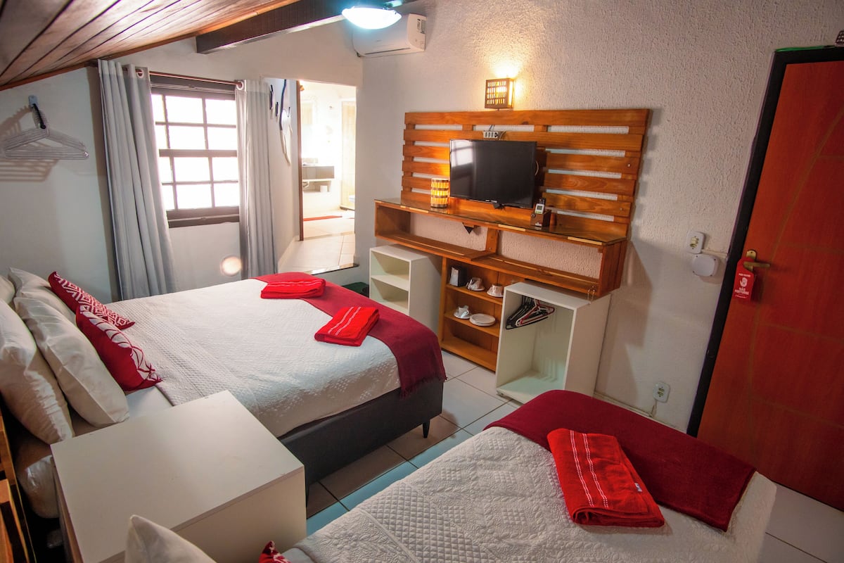 Habitación de hotel con dos camas, un televisor montado en un estante de madera, un escritorio y un armario.