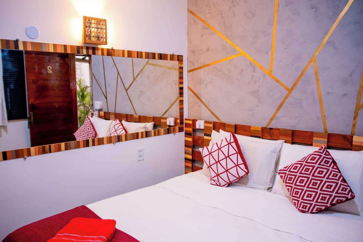 Habitación de hotel con un espejo grande, cabecera de madera y almohadas estampadas.