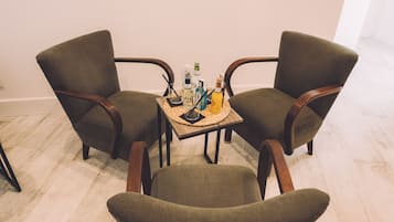 Two armchairs and a small table with a tray of bottles and a candle in a room with wooden flooring and plain walls.