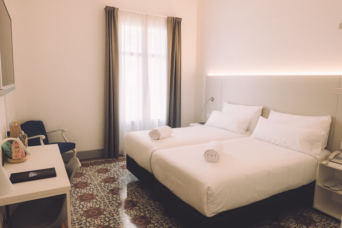 A hotel room with two beds, a desk, a chair, a telephone, and a window with curtains.