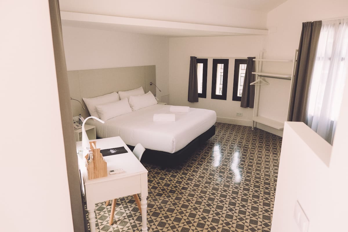 A hotel room with a bed, bedside table, and a desk.