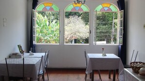 A dining area with two tables and chairs, a chandelier, and a view through a stained glass window. - Pousada Villa Real (Sabara)