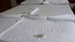 A neatly made bed with white linens and a towel with embossed text. - Pousada Villa Real (Sabara)