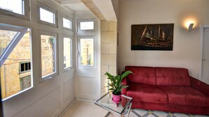 Una habitación con un sofá rojo, una mesa de vidrio con una planta en maceta y un cuadro de un velero en la pared.