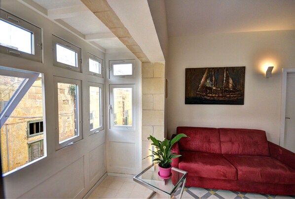 Una habitación con un sofá rojo, una mesa de vidrio con una planta en maceta y un cuadro de un velero en la pared.