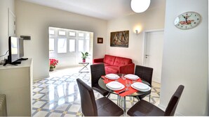 Un comedor con una mesa dispuesta para cuatro, un sofá rojo y un cuadro en la pared.