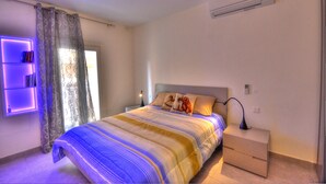 Un dormitorio con cama, mesita de noche, lámpara, aire acondicionado y una ventana con cortinas.