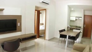 A modern living room with a flat-screen TV, a dining table with chairs, a sofa, and a kitchen area with cabinets and a countertop. - Marina Flat & Náutica Apartamento - Férias em Caldas Novas (Caldas Novas)