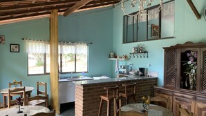 A kitchen with a central island, wooden chairs, a dining table, and a chandelier. - Pousada & Camping Serras Verdes (Valenca)