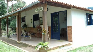A building with a covered porch, a reception area, and a blue door. - Pousada & Camping Serras Verdes (Valenca)