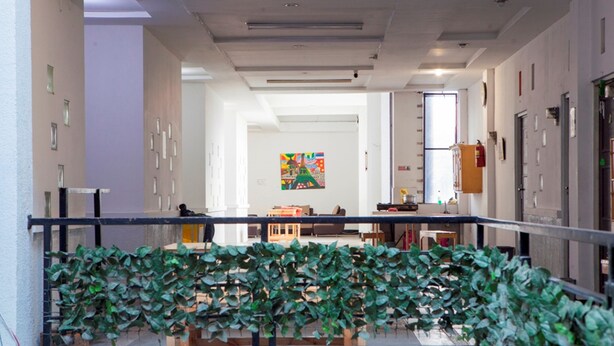 Un hall d’entrée spacieux au design moderne, agrémenté d’une barrière végétale, d’un extincteur et d’une œuvre d’art colorée accrochée au mur.