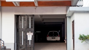 Une voiture est garée à l’intérieur d’un bâtiment, derrière une grille métallique, et un panneau est fixé au mur.