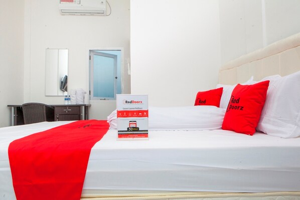 A hotel room with a bed, a desk, a chair, a mirror, and a door.