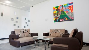 Un salon moderne avec deux canapés et une table basse en verre, un tableau coloré représentant la Tour Eiffel au mur et un plafond blanc doté d’un éclairage encastré.