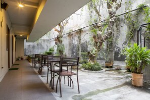 A covered outdoor seating area with tables and chairs, surrounded by potted plants and trees. - RedDoorz Plus near Asia Afrika 3 (Bandung)