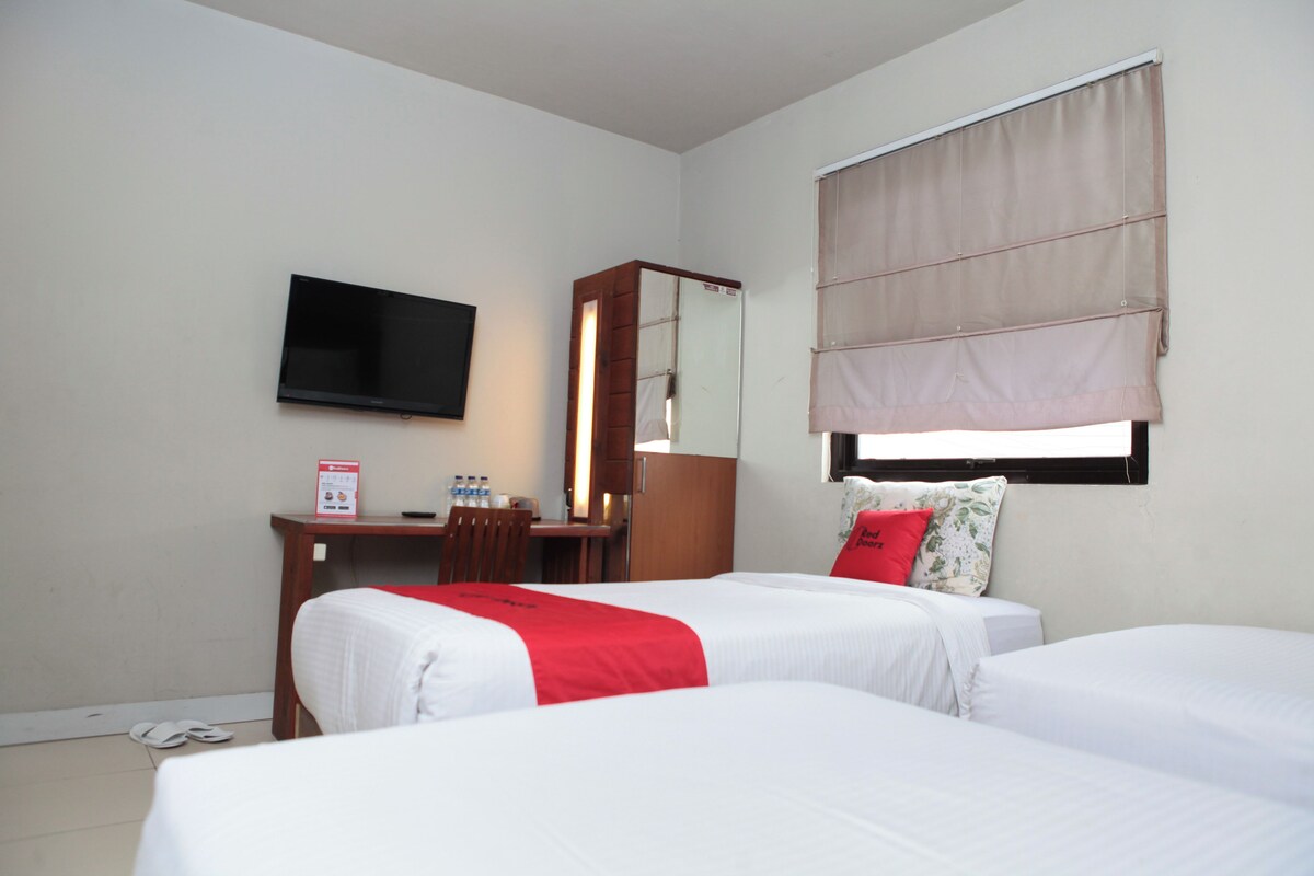 A hotel room with two beds, a desk, a chair, a TV, and a window with a blind.